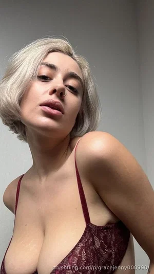 Woman with short blonde hair in red lace top, posing indoors.