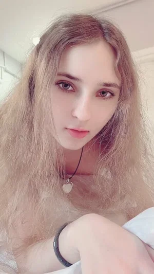 Long-haired blonde woman with heart necklace in bed.