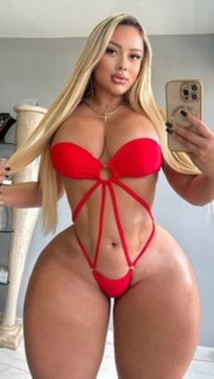 Woman with long blonde hair in red strappy bikini taking mirror selfie indoors.