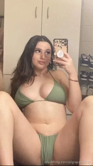 Woman in green bikini taking mirror selfie in indoor setting.