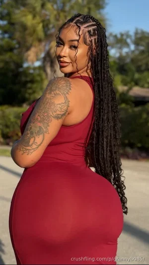Woman in red bodycon dress, long braids, tattooed arm, outdoors.