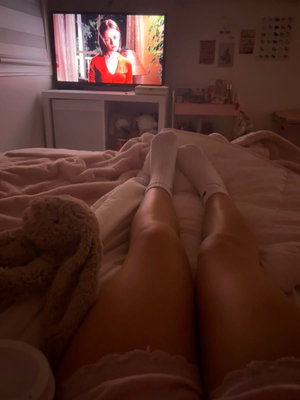 Person's legs in bed with white socks and pink shorts in bedroom.
