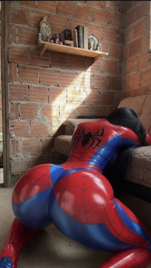 Person in Spider-Man bodysuit posing on floor near brick wall and couch.