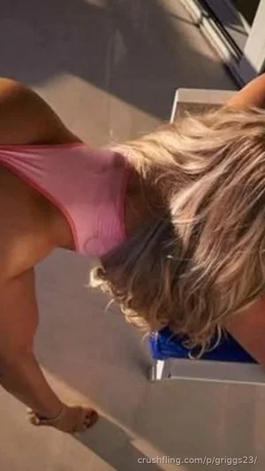 Woman with blonde hair in pink top bending forward, outdoor setting.