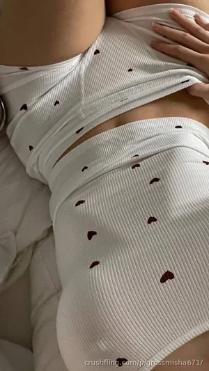 Woman in white heart-patterned ribbed top, lying on bed, midriff exposed.