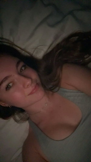 Woman with brown hair in tank top lying on bed.