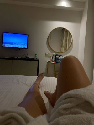 Person's legs on bed covered by white towel in bedroom.