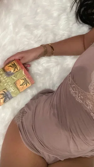 Woman in beige lace lingerie lying on white fluffy surface, holding a small box.
