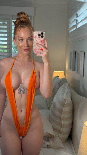 Woman in orange halter swimsuit takes mirror selfie in bedroom.