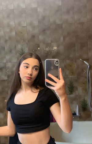 Slim woman in black crop top taking bathroom mirror selfie.