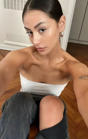 Woman with dark hair in white top and jeans sitting indoors.