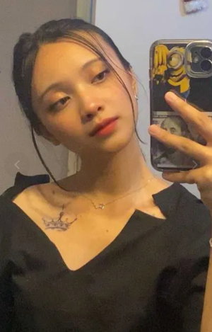 Asian woman with dark hair in black top taking indoor selfie.