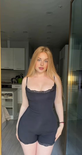 Blonde woman in dark gray lace romper in modern kitchen.