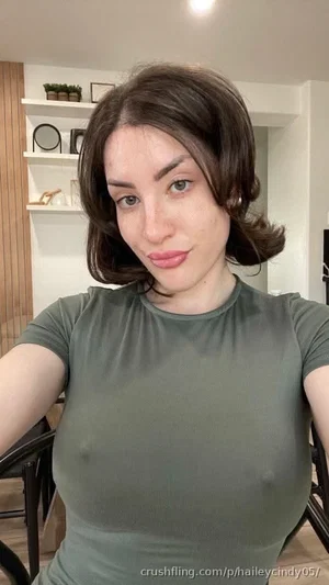 Woman with short brown hair in olive green top, sitting indoors in a room with shelves.