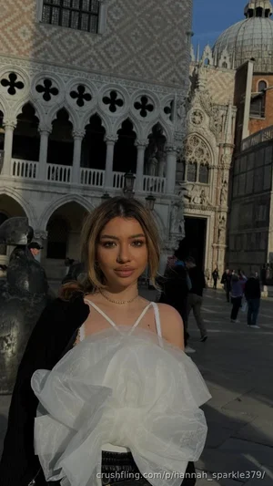 Woman in white ruffled top and black jacket, standing in front of ornate European architecture.