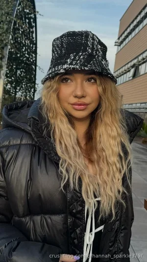 Woman with long blonde hair wearing black puffer jacket and bucket hat outdoors.