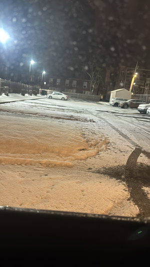 Snowy urban parking lot at night with cars and buildings.
