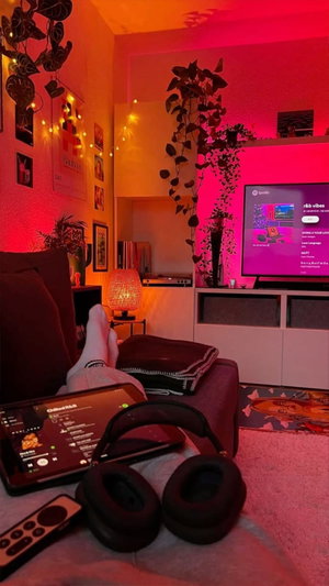 Legs in socks on couch in red-lit room with plants and TV.
