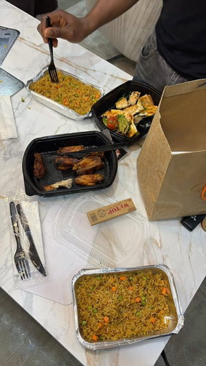 Person eating takeout food at a marble table with containers and utensils.