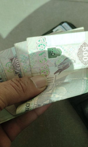Hand holding a stack of 500 denomination banknotes.
