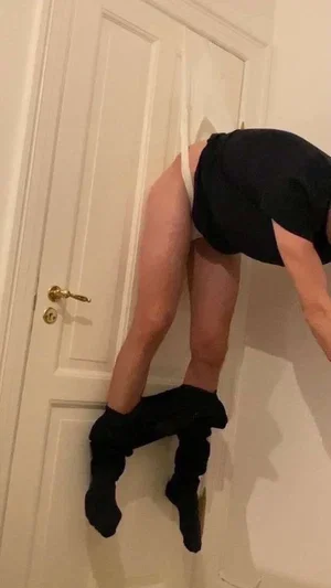 Person in black top and socks bending over near a white door indoors.