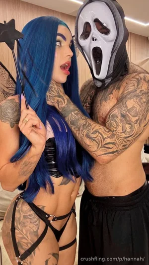 Woman with blue hair and tattoos in black lingerie, posing with a masked man with tattoos in a
