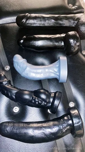 Five black and gray silicone dildos arranged on a black leather surface.