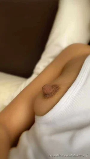 Woman with bare breast partially covered by white top, lying in bed.