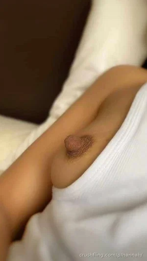 Woman with bare breast and nipple visible under white top, lying on bed.