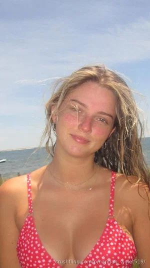 Woman in red polka-dot bikini top, blonde hair, smiling by the ocean.