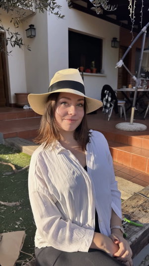 Woman in white shirt and hat sitting outdoors near a patio.