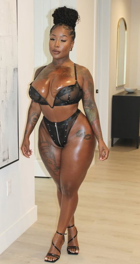 Curvy black woman in black lingerie standing indoors.