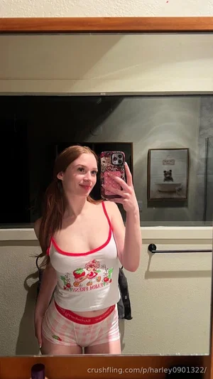 Woman in white tank top and pink shorts takes mirror selfie in bathroom.