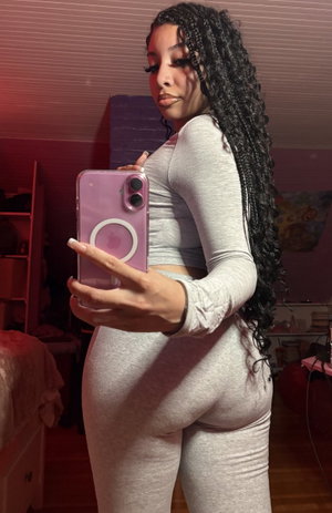 Curvy woman with braids in gray top and leggings, bedroom selfie.