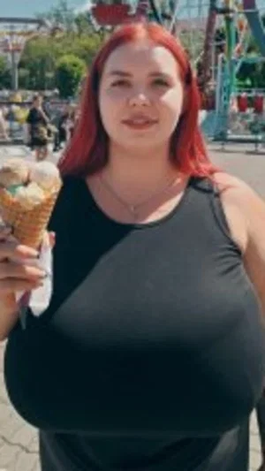 Woman with red hair in black top holding ice cream at amusement park.