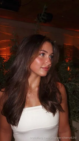 Woman with long dark hair in white strapless top, indoors with plants and warm lighting.