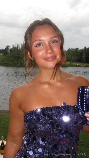 Woman in blue sequined strapless dress holding glass, outdoors by lake.