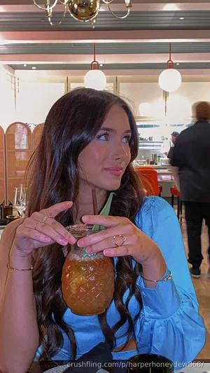 Woman with long dark hair in a blue top holding a pineapple drink in a restaurant.