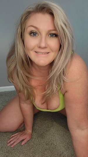Woman with blonde hair in green top kneeling on carpet indoors.