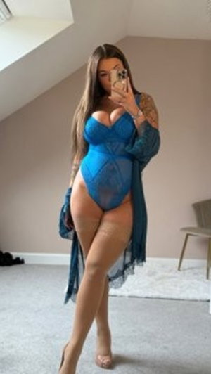 Woman in blue lace bodysuit and sheer robe, taking mirror selfie in bedroom.