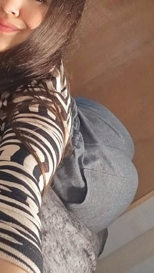 Woman with long dark hair in striped top and gray pants, posing indoors.
