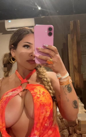 Woman in orange floral halter top with braided hair, taking mirror selfie indoors.