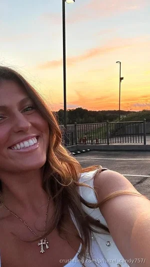 Woman with long brown hair in white top smiling at sunset in parking lot.