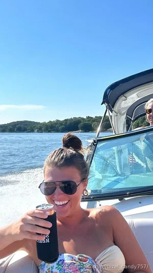 Woman in floral top and sunglasses on a boat, holding a can, smiling.