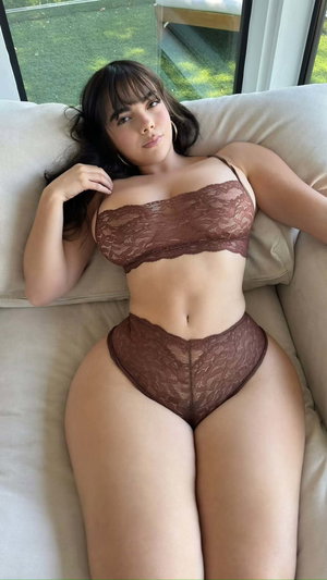 Woman in brown lace lingerie reclining on couch indoors.
