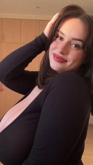 Brunette woman in black top posing indoors with hand in hair.