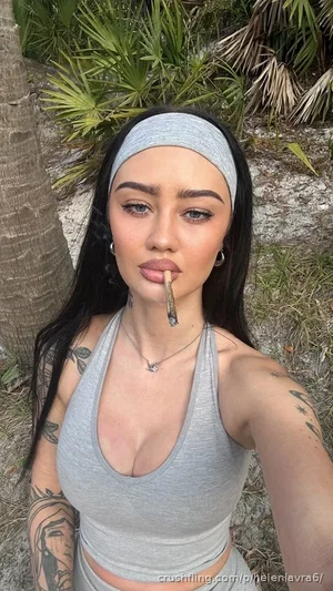 Woman with tattoos in gray crop top and headband, outdoors near palm trees.