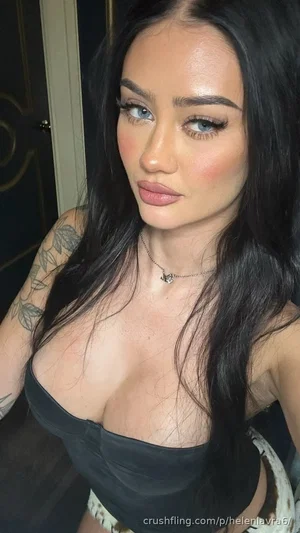 Woman with long dark hair and tattoos wearing a black strapless top indoors.