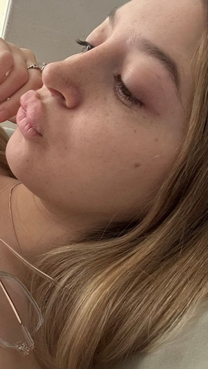 Blonde woman with freckles lying down eyes closed wearing glasses.