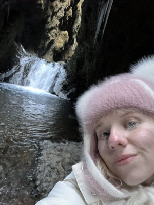Woman in pink hat taking selfie by waterfall in cave.